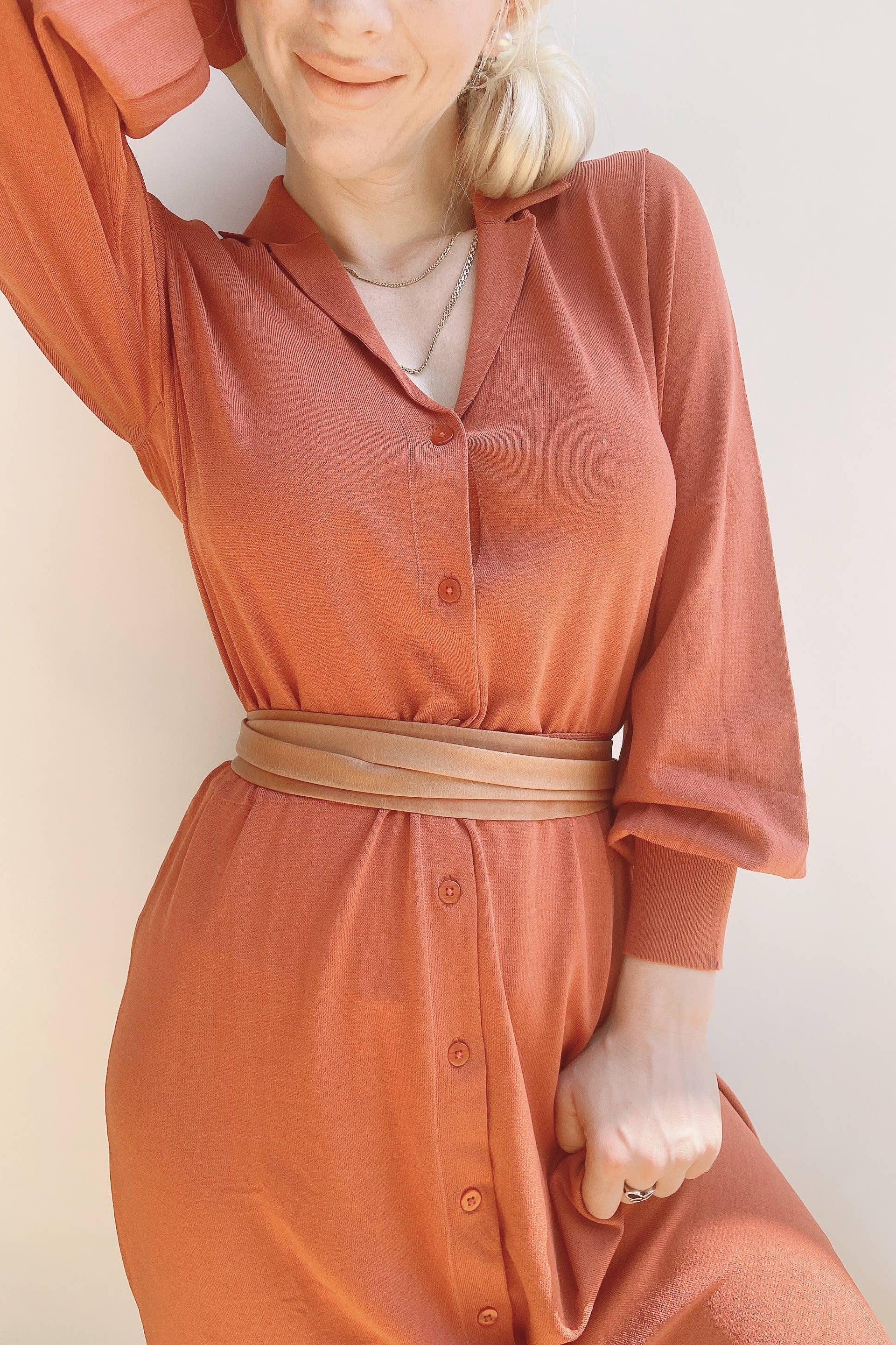 Person wearing a long rust-colored dress with a belt against a light background