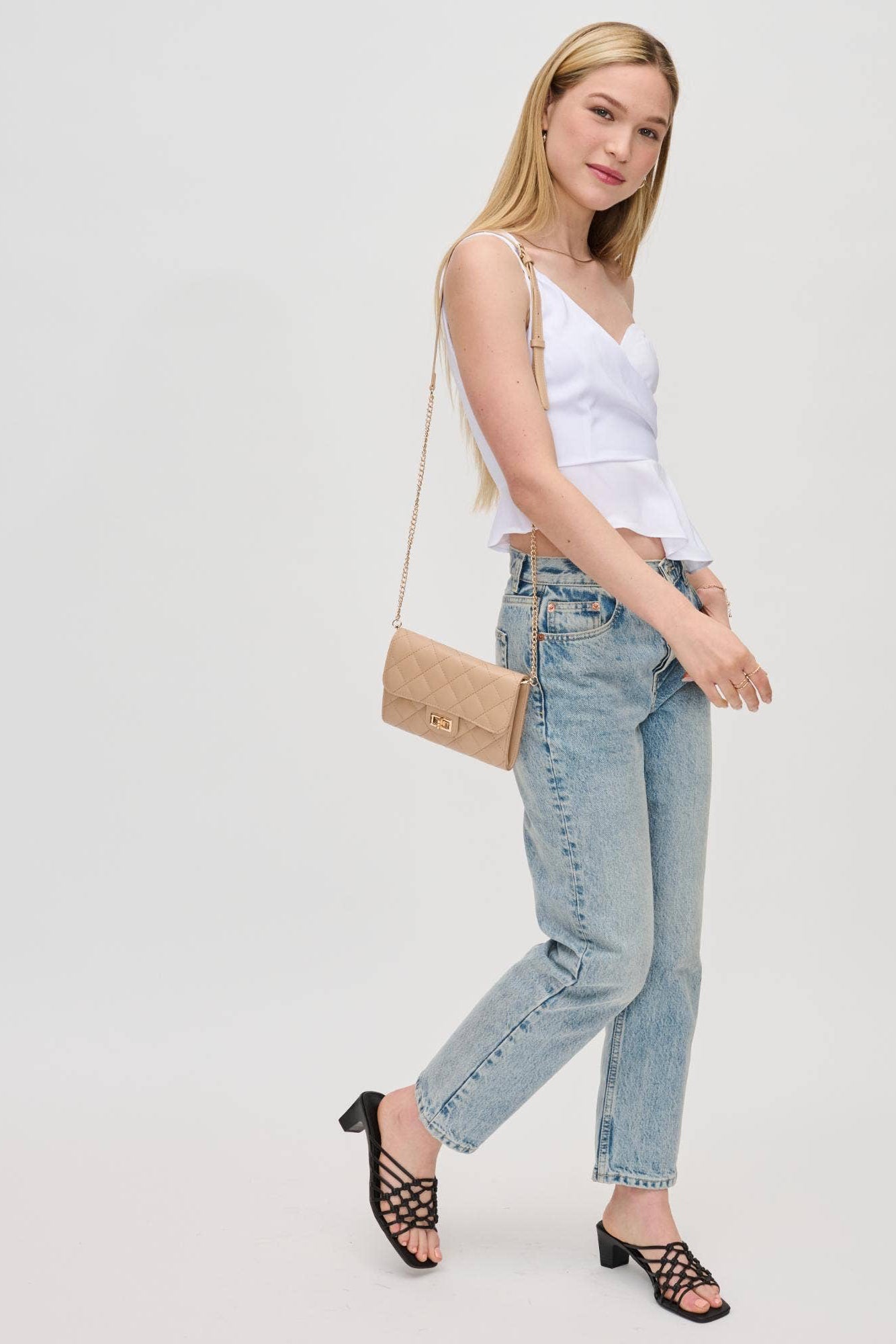 Woman wearing a white top and light blue jeans with a beige handbag on a plain background
