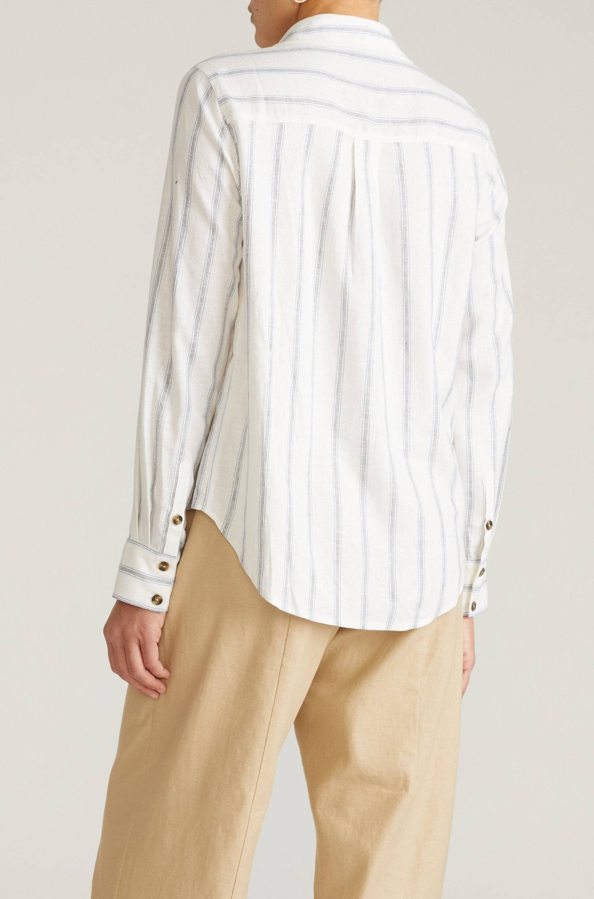 Person wearing a white striped shirt and beige pants on a plain background