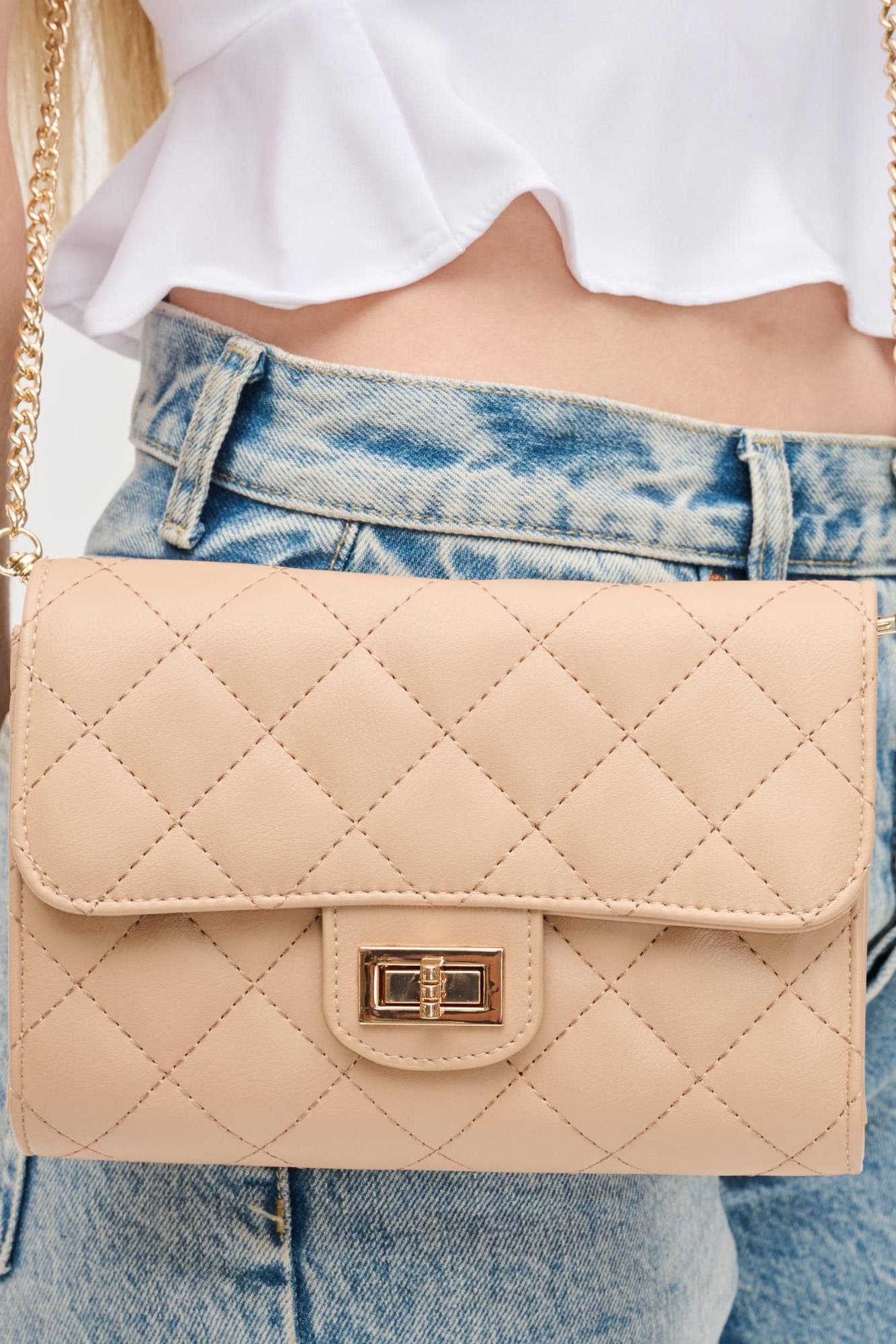 Beige quilted handbag with gold chain strap worn by a person in jeans and a white top.