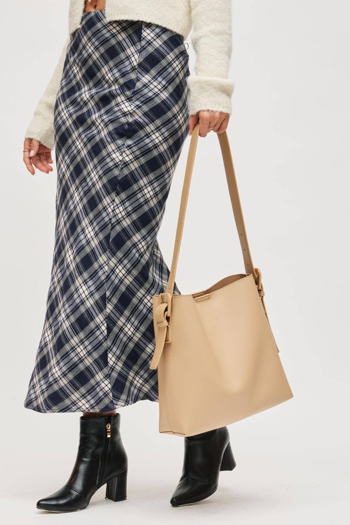 Person wearing a plaid skirt and holding a beige tote bag on a white background