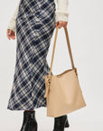Person wearing a plaid skirt and holding a beige tote bag on a white background