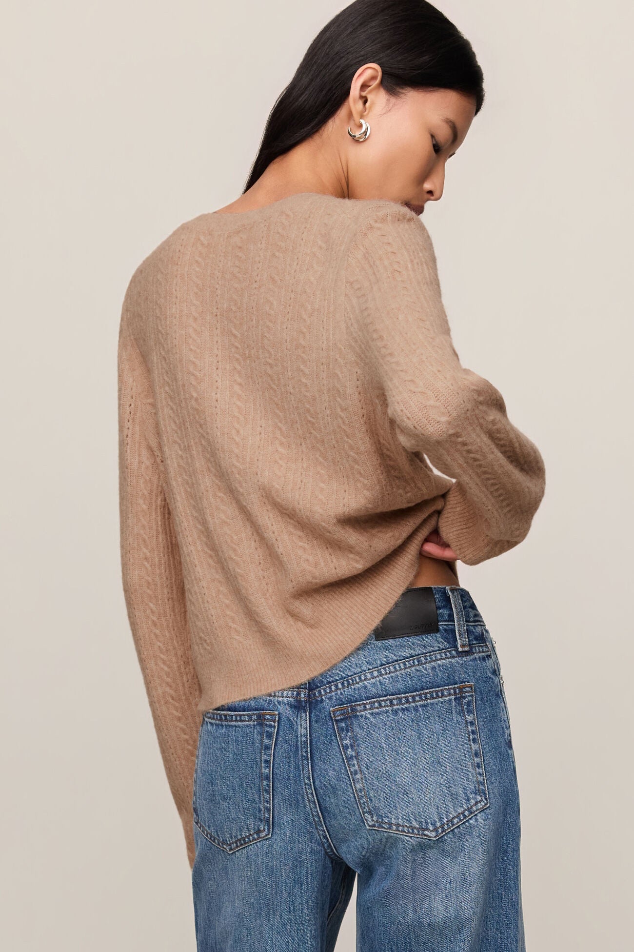 Person wearing a beige sweater and blue jeans against a plain background