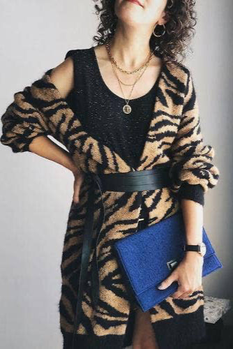 Person wearing a black and brown patterned cardigan holding a blue clutch against a neutral background