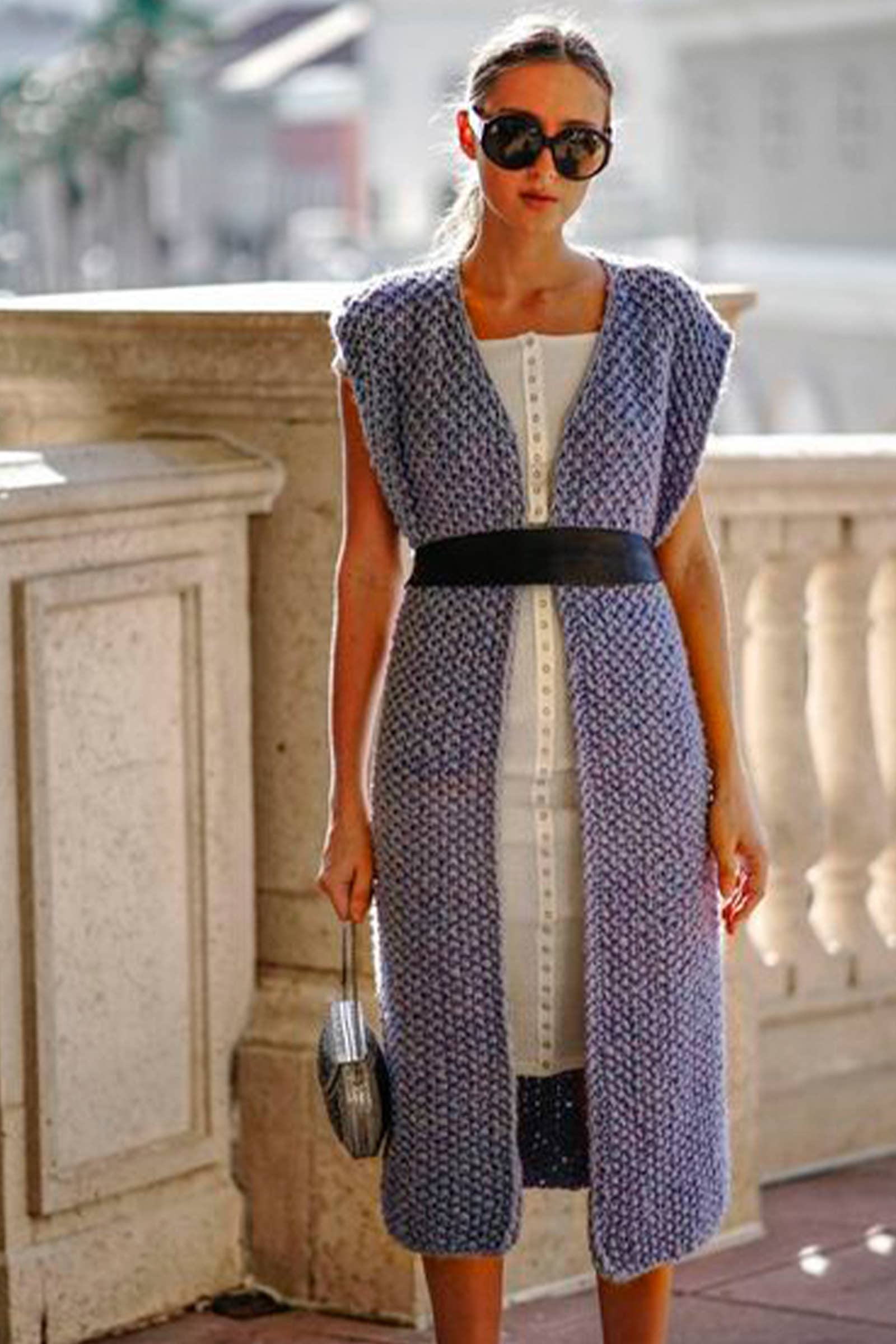 Woman wearing a long, patterned dress with a belt in an outdoor setting.