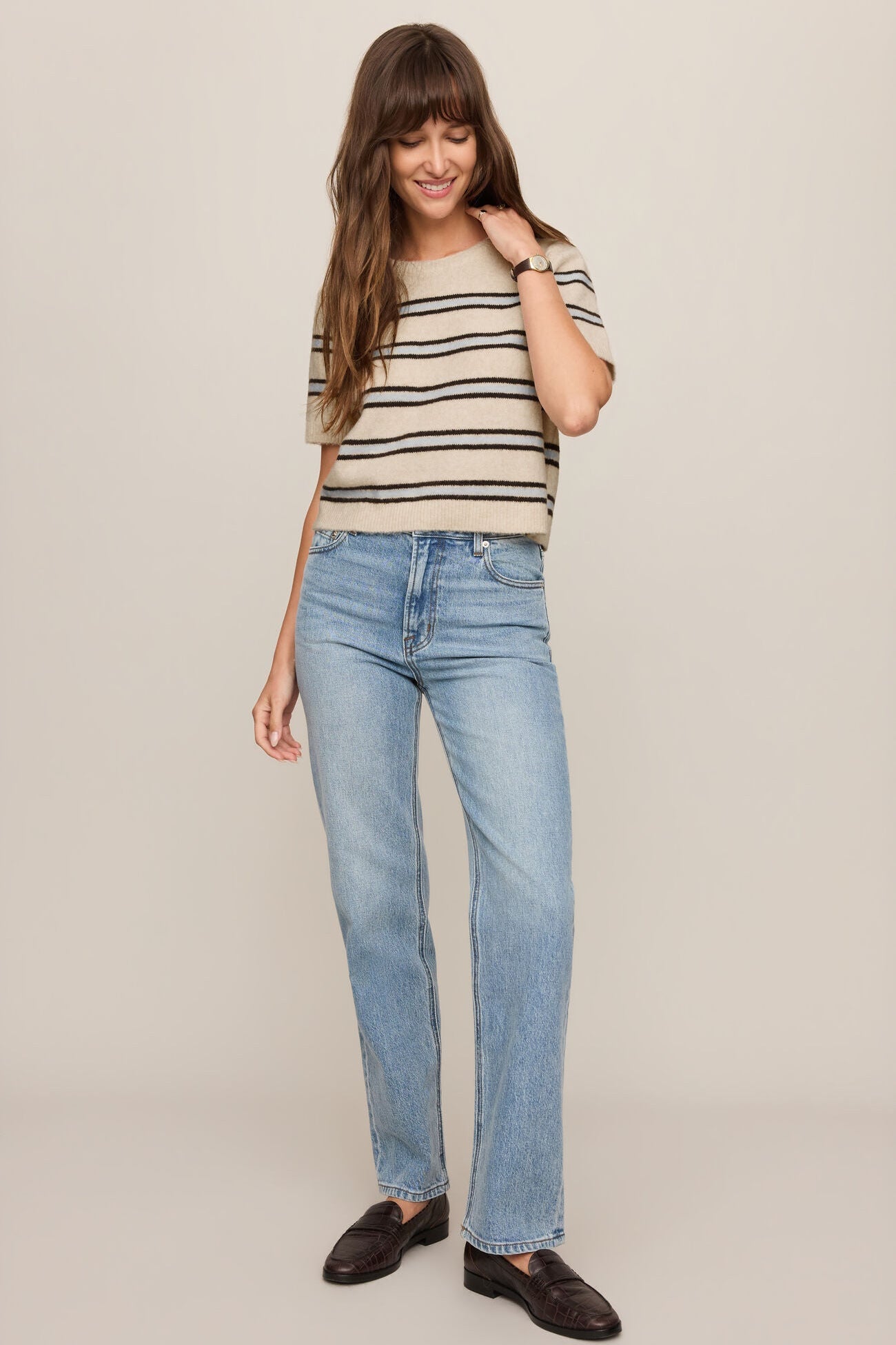 Woman wearing a striped shirt and blue jeans on a plain background