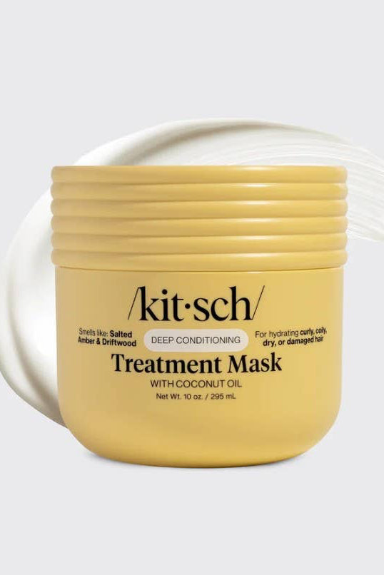 A yellow jar of kit'sch Treatment Mask with coconut oil, shown on a light gray background with a white cream smear behind it.