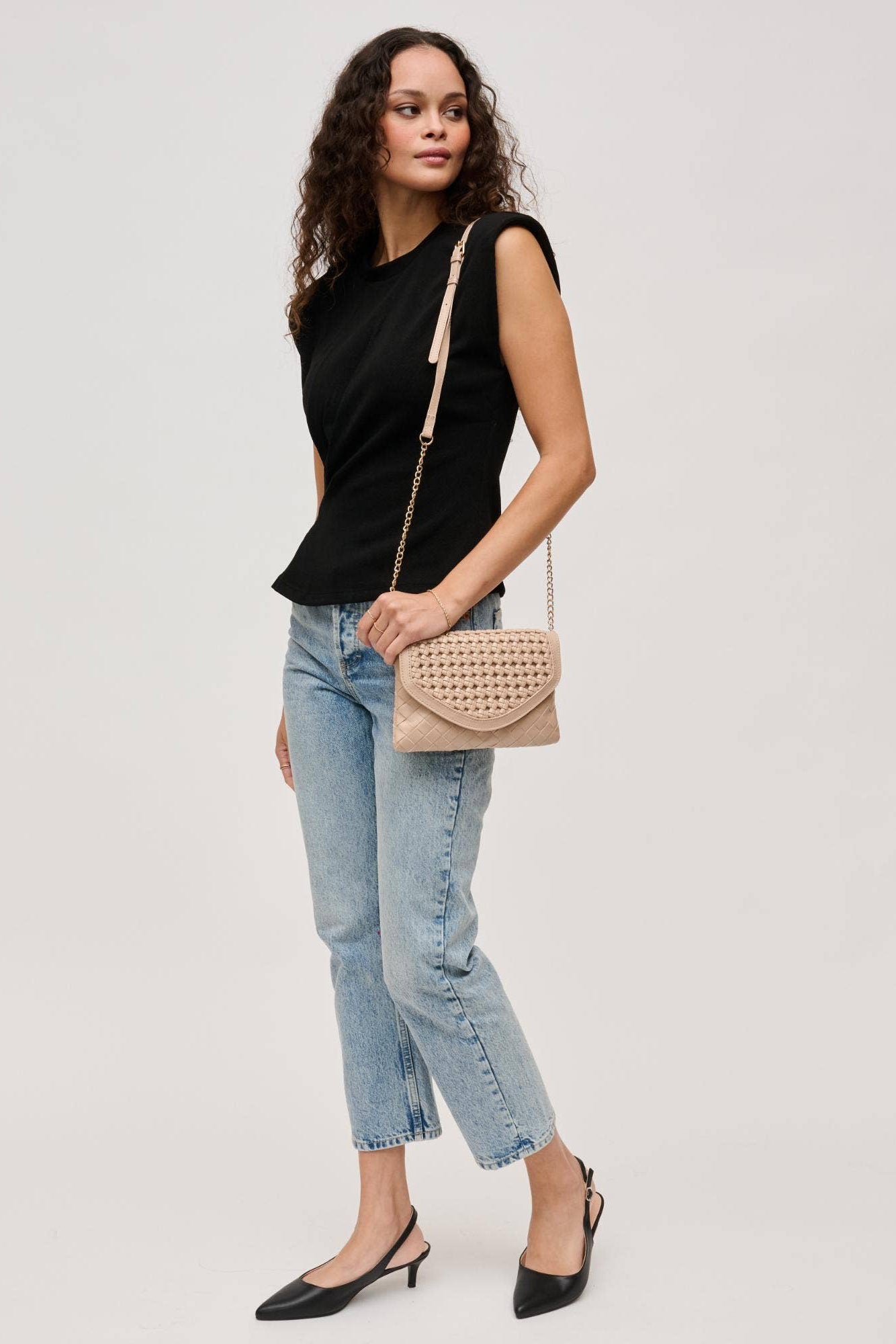 Woman wearing a black top and blue jeans, holding a beige handbag on a light gray background