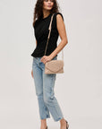 Woman wearing a black top and blue jeans, holding a beige handbag on a light gray background