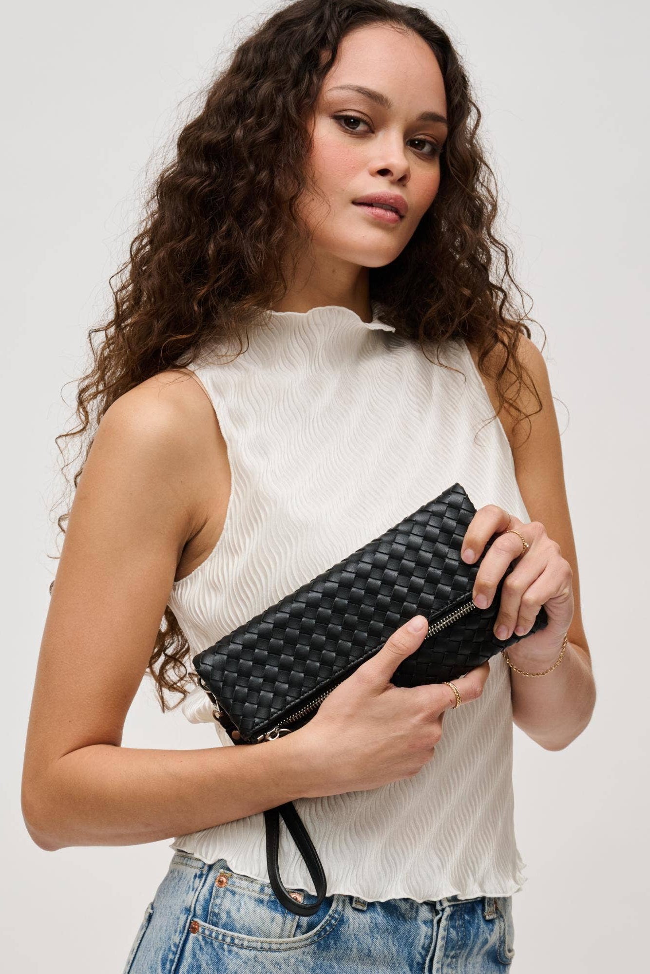 Woman holding a black woven clutch against a plain background