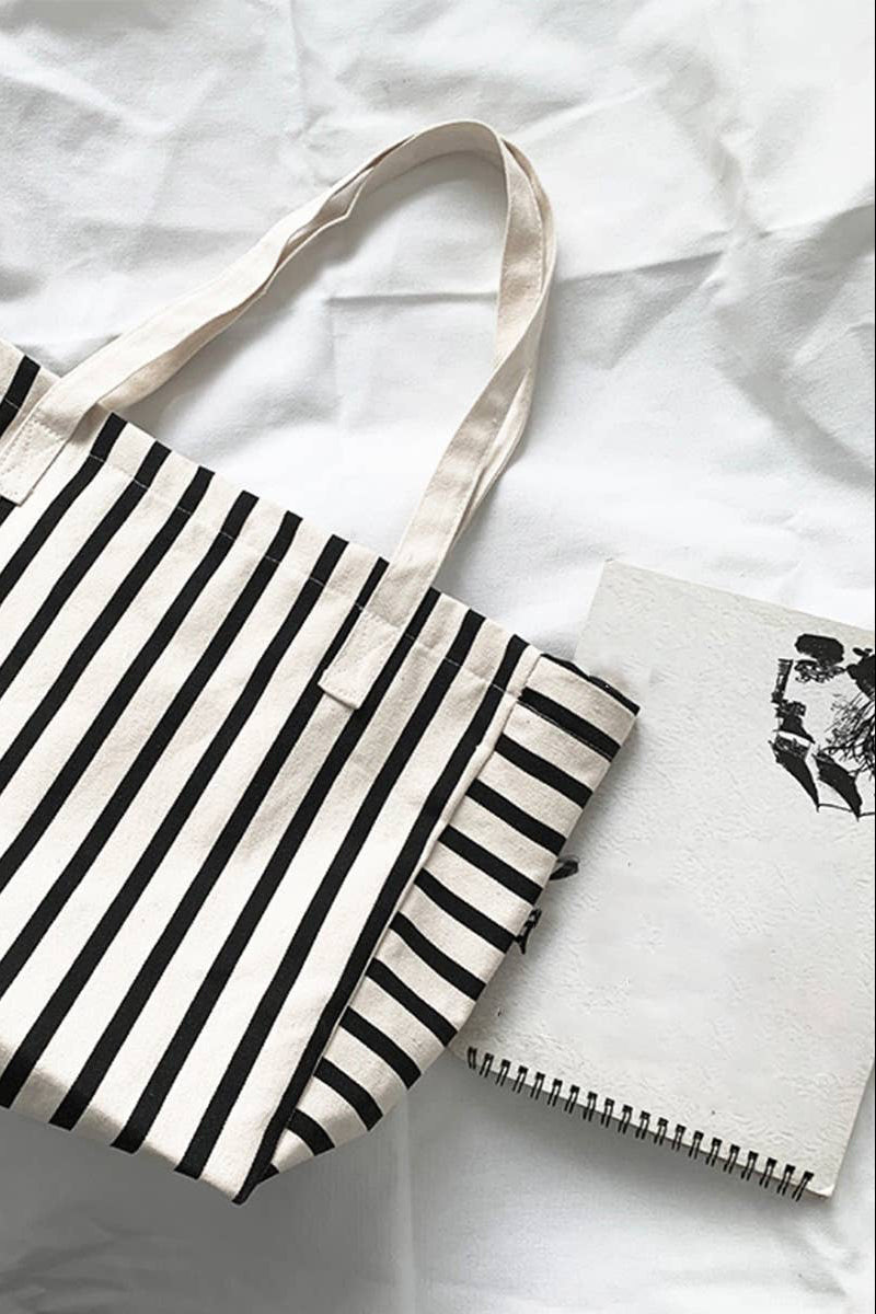 Black and white striped tote bag on a white surface with a notebook.