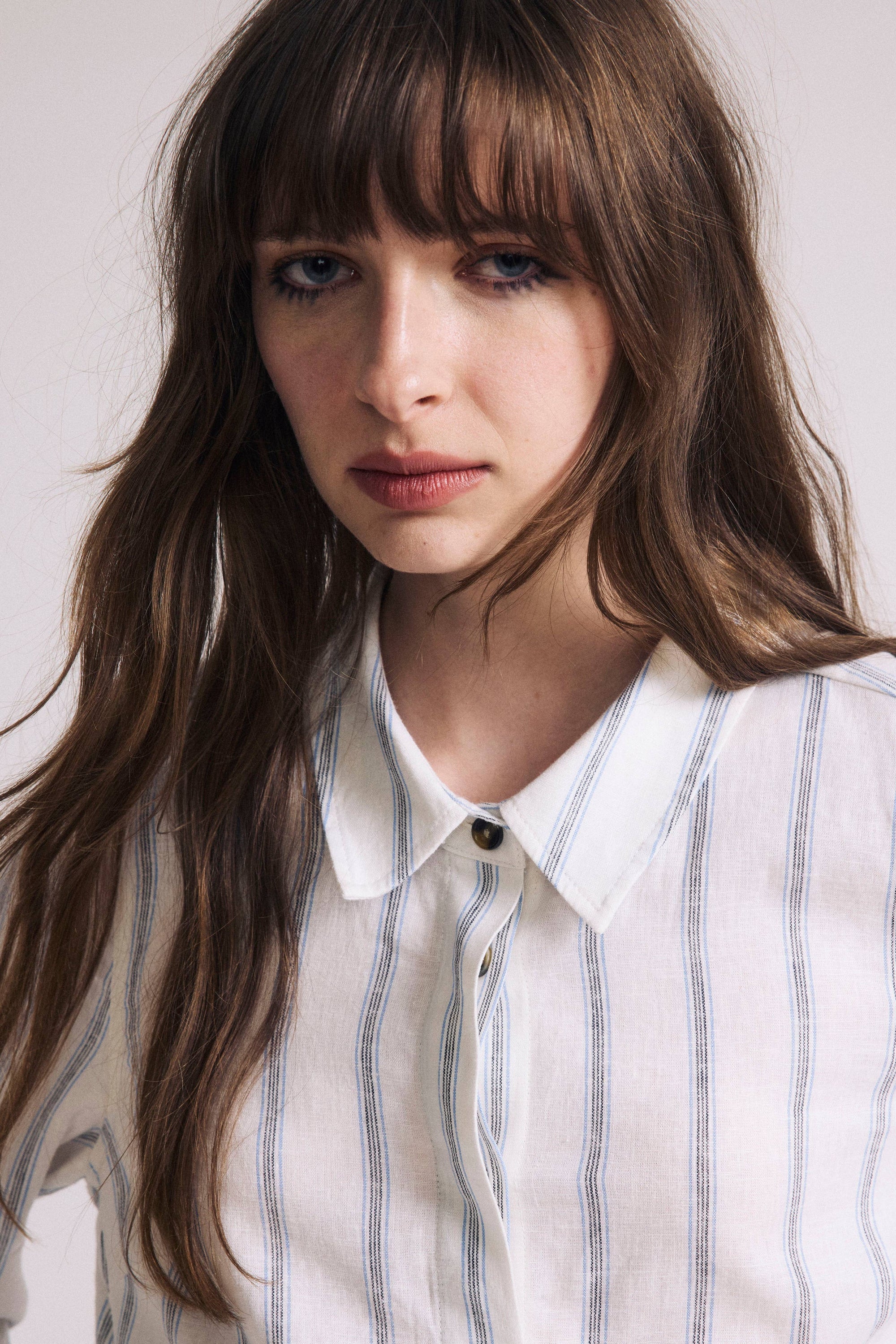 Woman wearing a white shirt with blue stripes against a plain background