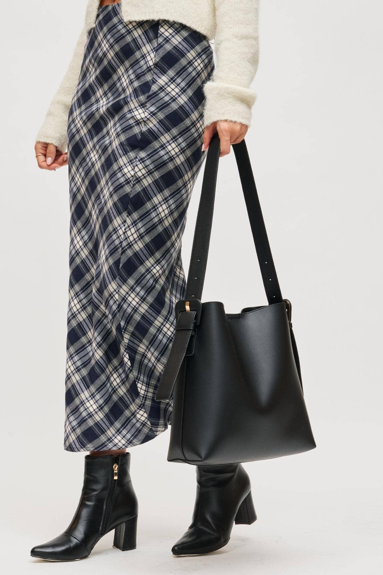Person holding a black handbag wearing a plaid skirt and black boots on a white background