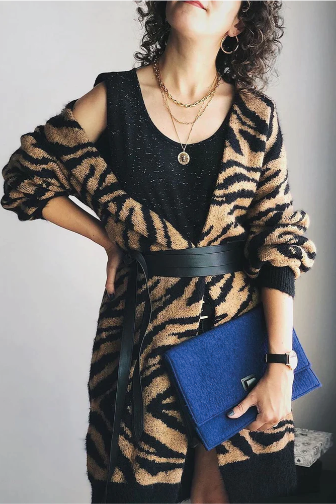 Person wearing a tiger-striped cardigan holding a blue clutch against a neutral background