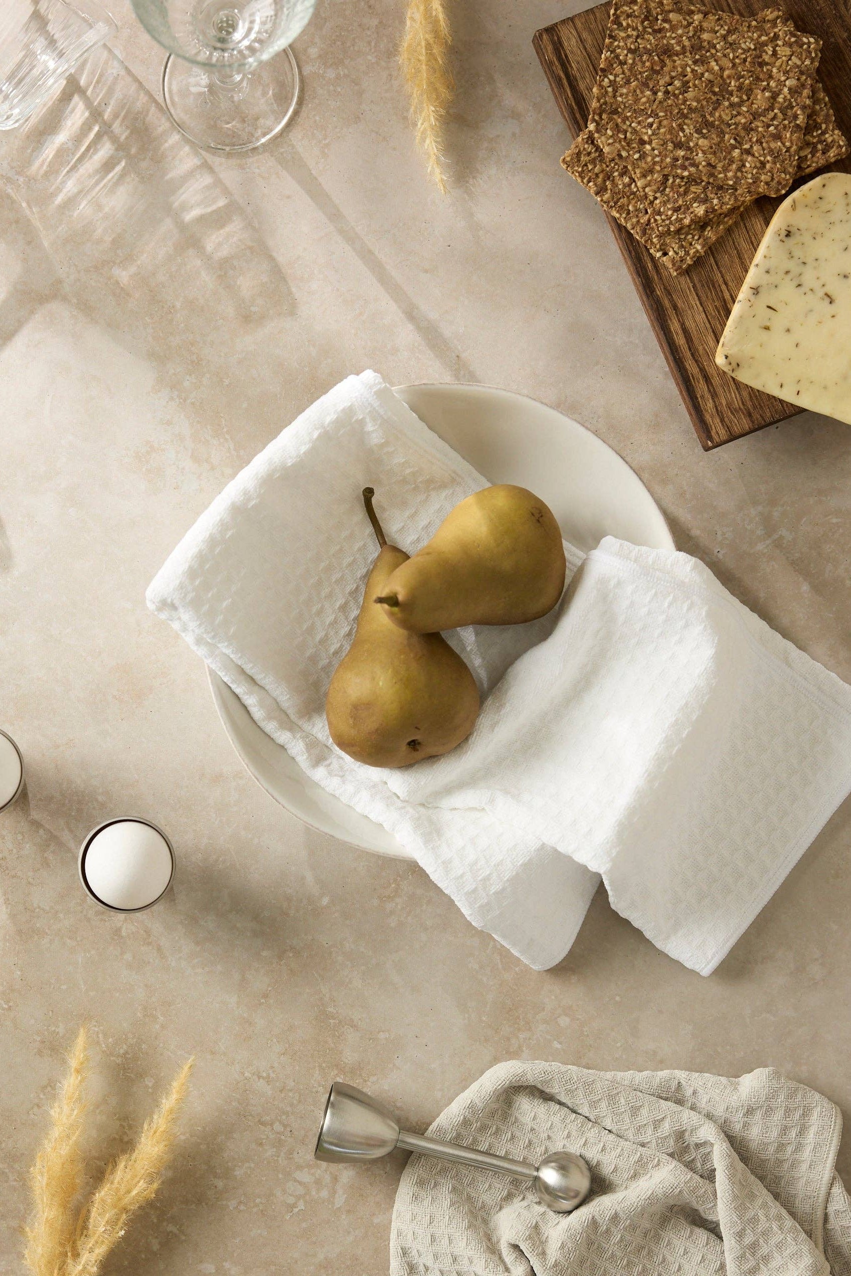 Two pears in a white bowl on a beige surface with bread and glasses.