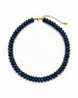 A dark navy blue beaded collar necklace with a gold clasp and extender chain, displayed on a clean white background.