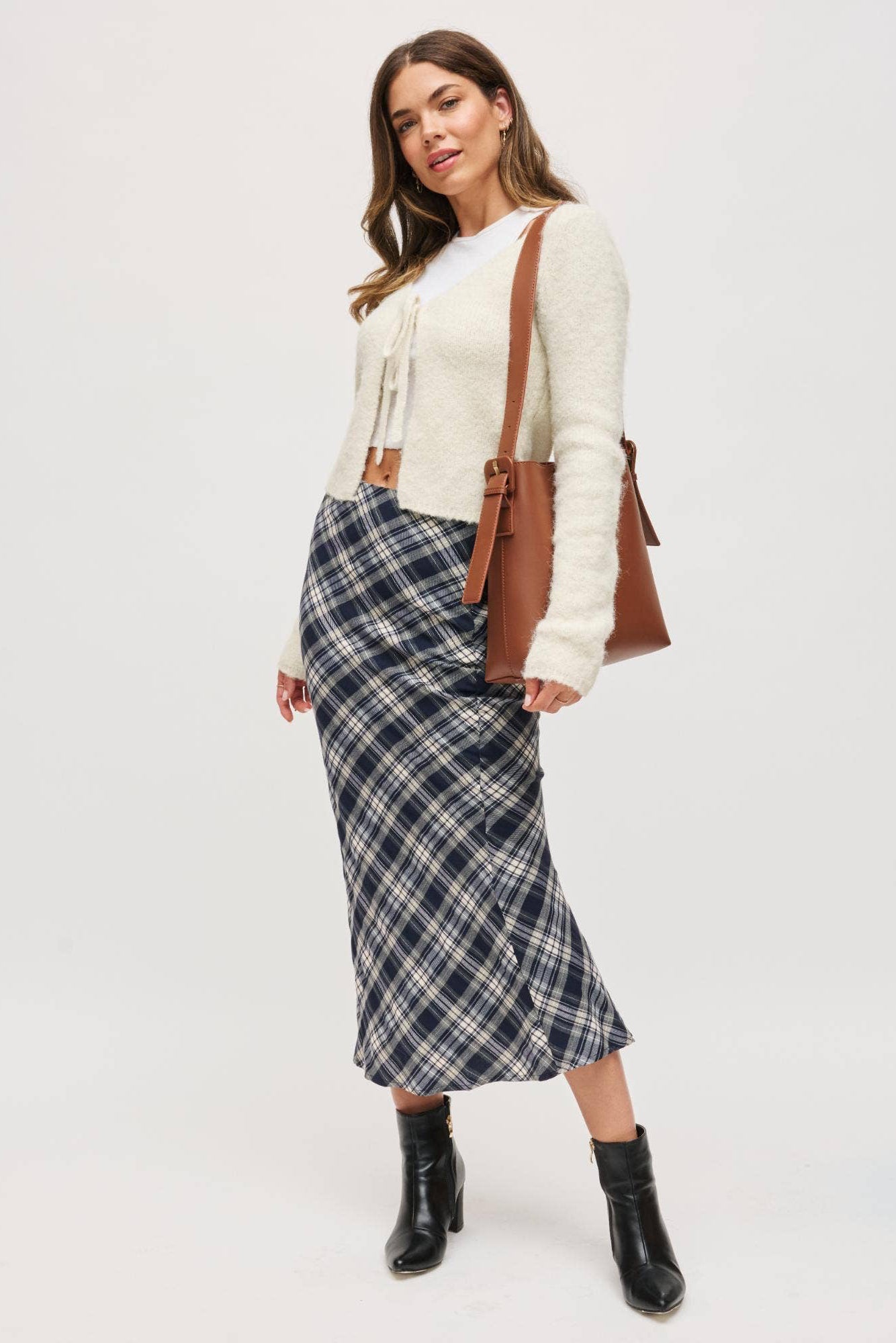 Woman wearing a plaid skirt, white sweater, and black boots on a white background