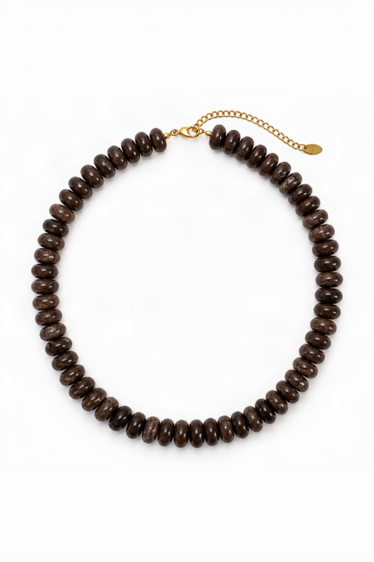 A dark brown beaded necklace made of small, polished disc-like beads, featuring a gold-tone chain extender clasp with a small tag, displayed on a clean white background.