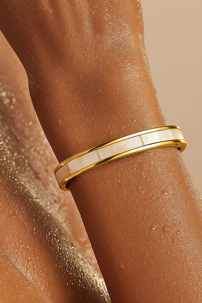 Gold bracelet on a wrist with a neutral background