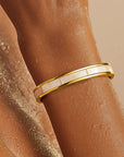 Gold bracelet on a wrist with a neutral background