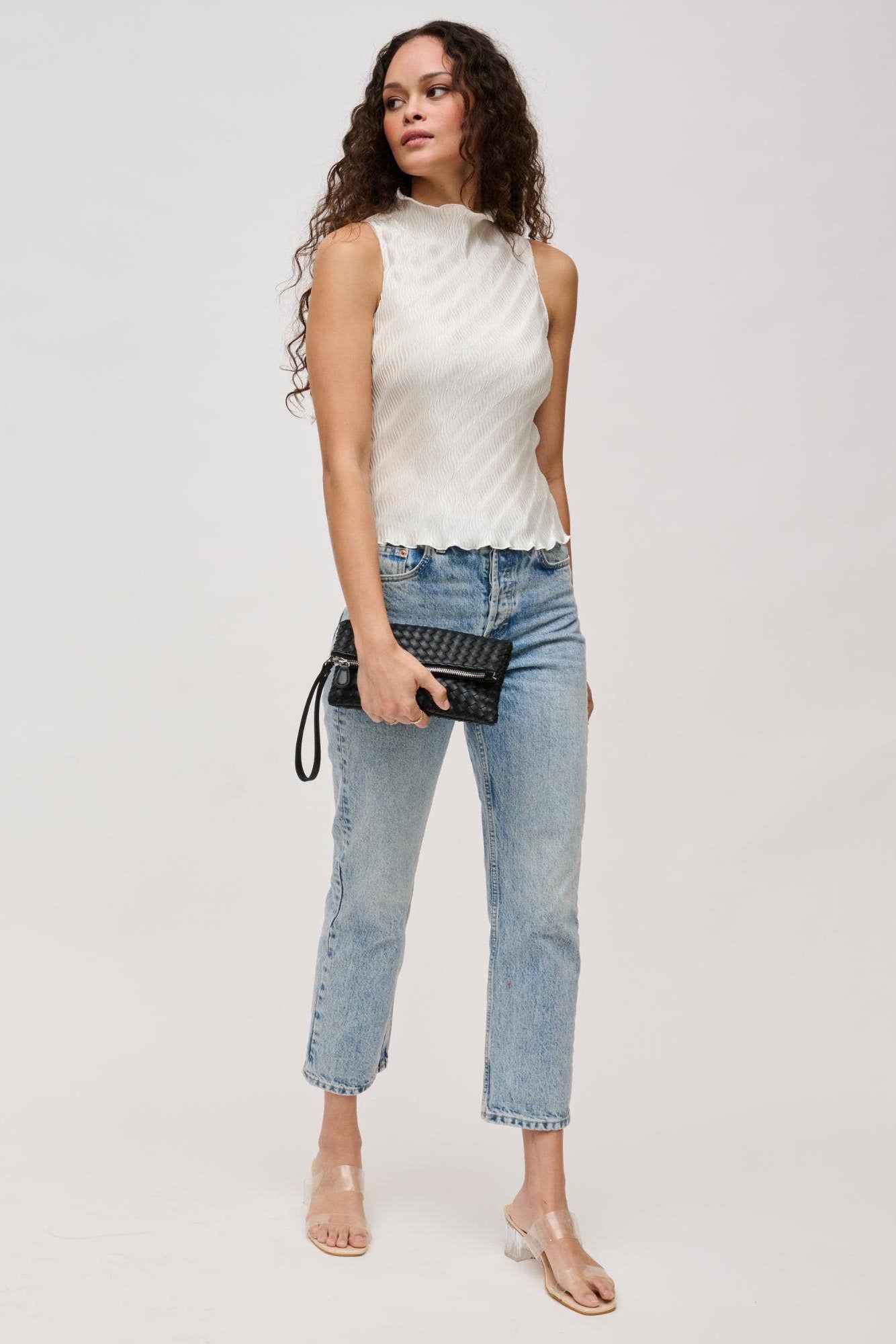 Woman wearing a white sleeveless top and blue jeans on a plain background