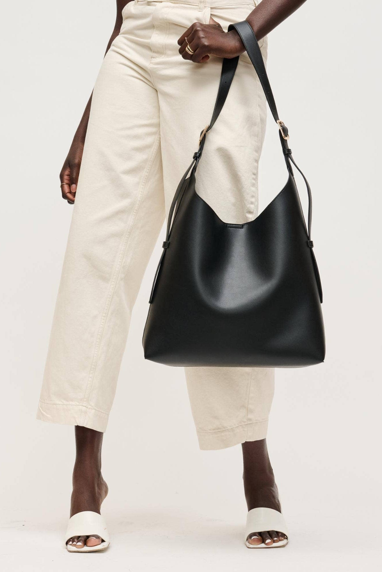Person holding a black leather handbag against a white background