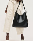 Person holding a black leather handbag against a white background