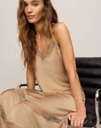 Woman wearing a beige dress sitting on a chair against a plain background