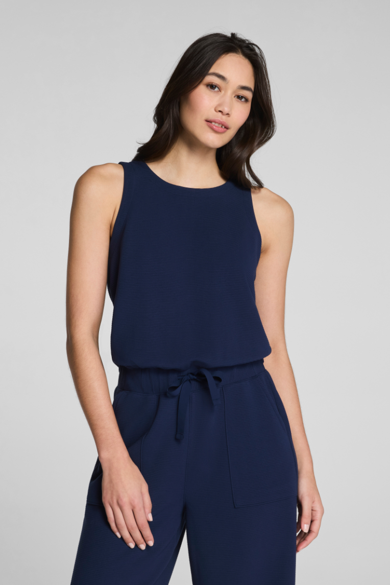 Woman wearing a navy blue sleeveless top and pants on a gray background