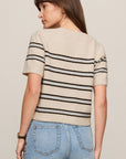 Woman wearing a beige sweater with black stripes and blue jeans on a plain background