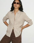 Woman wearing a beige shirt and brown pants against a white background