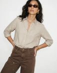 Woman wearing a beige shirt and brown pants with sunglasses on a white background