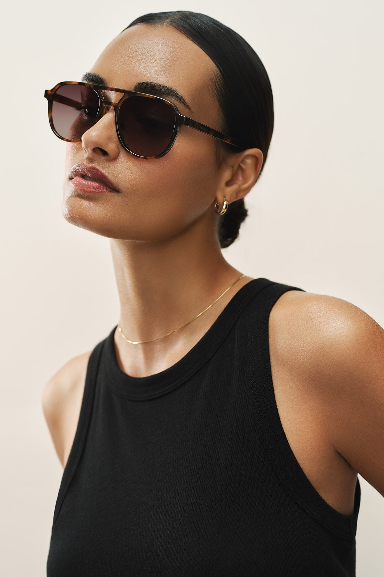Woman wearing sunglasses and a black tank top against a neutral background