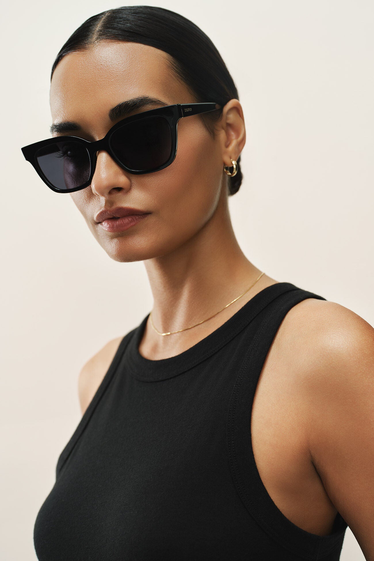 Woman wearing black sunglasses and a black top against a beige background