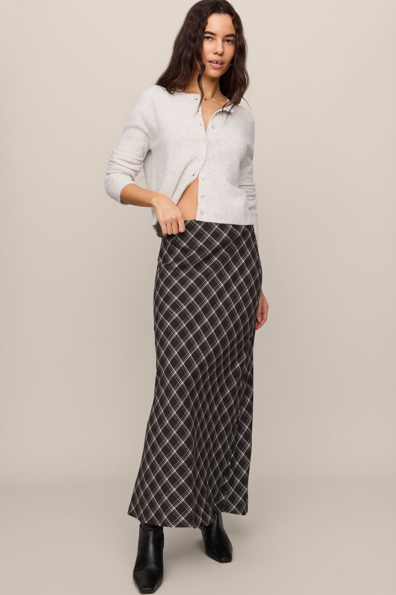 Woman wearing a white cardigan over a black and white checkered dress on a beige background
