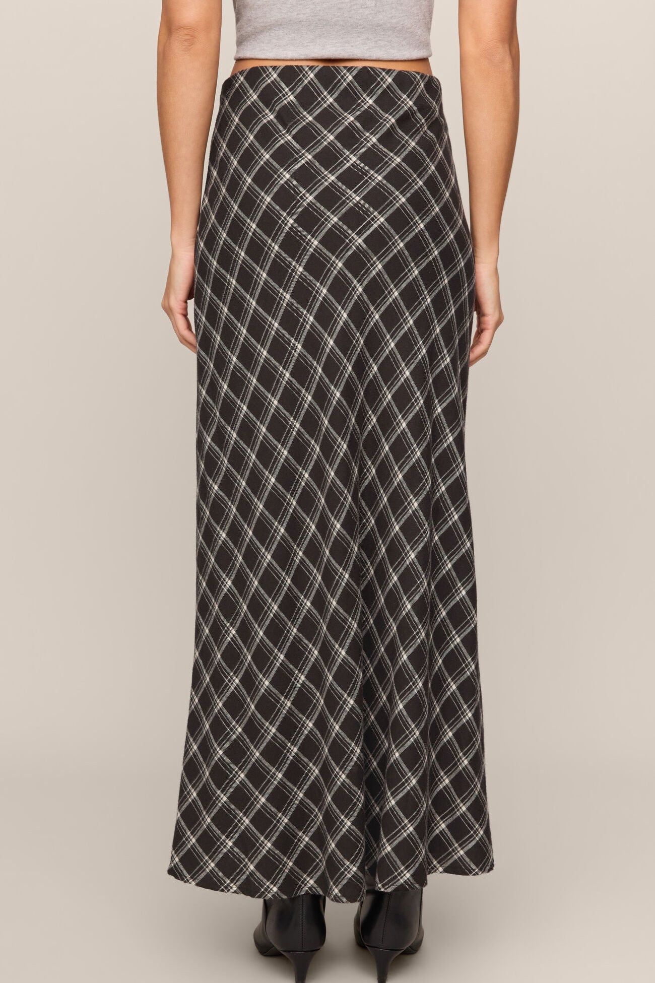 Person wearing a long plaid skirt on a neutral background