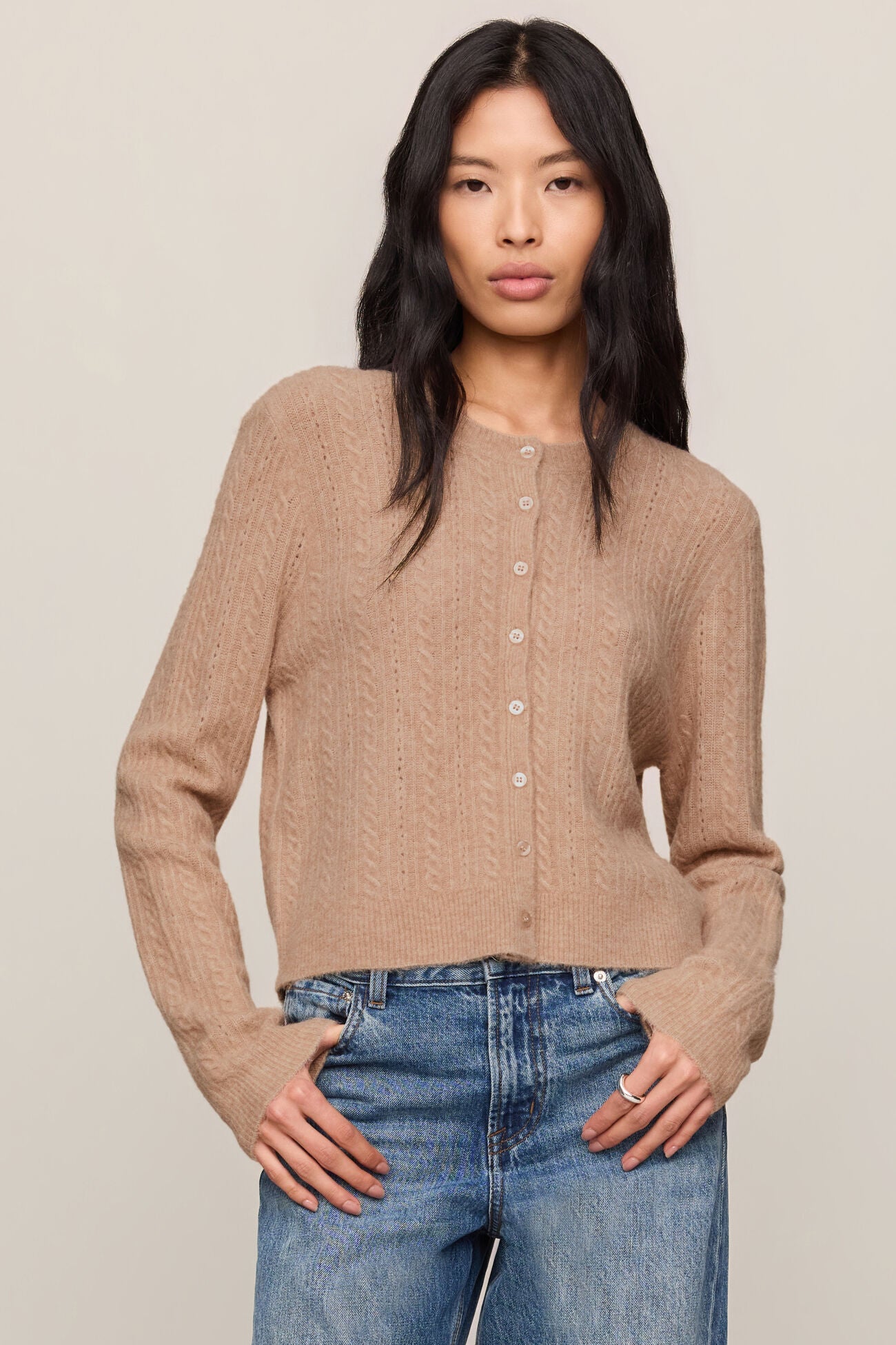 Woman wearing a beige cardigan and blue jeans against a plain background