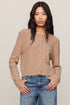 Woman wearing a beige cardigan and blue jeans against a plain background
