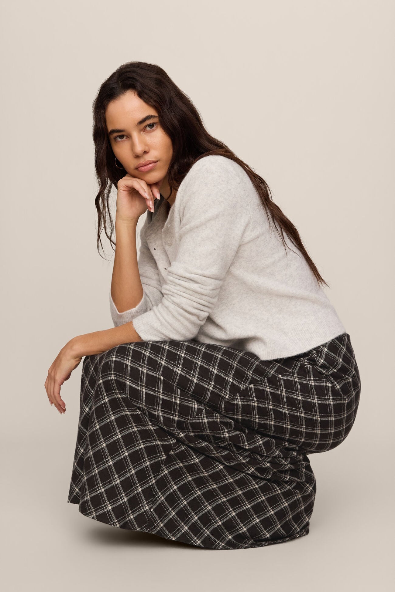 Woman wearing a white sweater and black plaid pants sitting on a beige background
