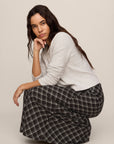 Woman wearing a white sweater and black plaid pants sitting on a beige background
