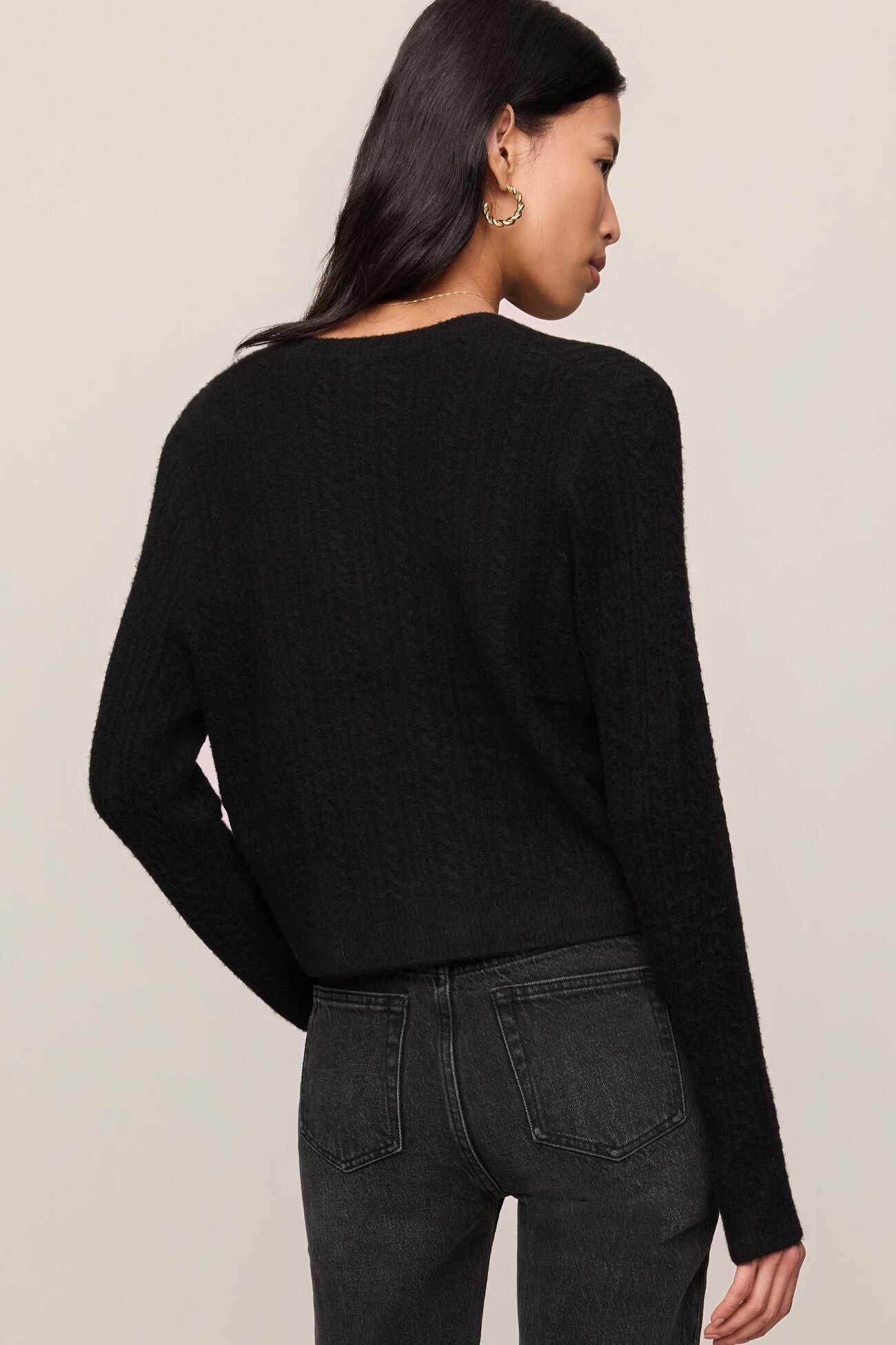 Person wearing a black sweater and dark jeans against a plain background