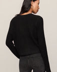 Person wearing a black sweater and dark jeans against a plain background