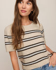 Woman wearing a beige and black striped sweater with blue jeans against a plain background