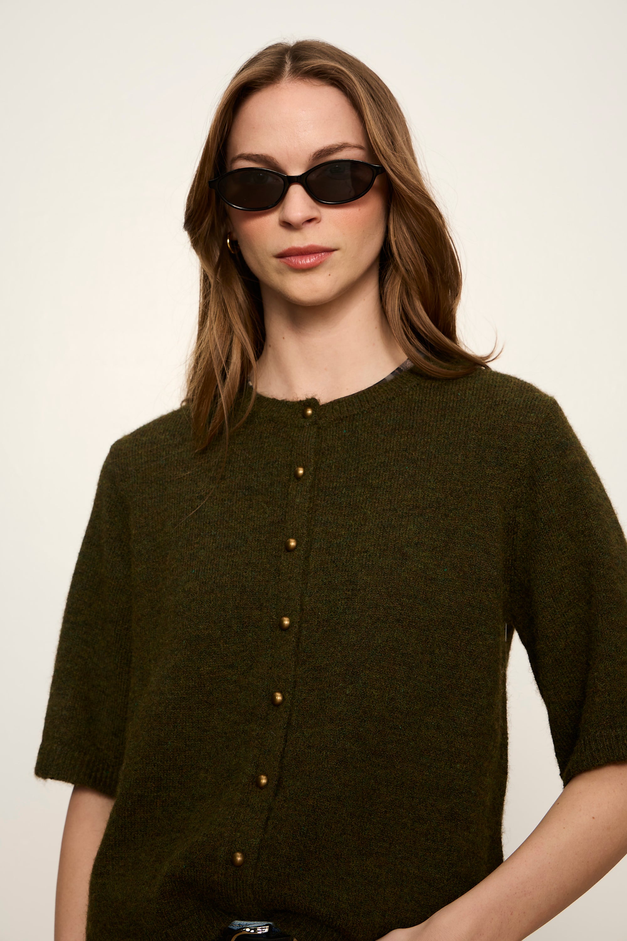 Woman wearing a dark green button-up shirt with a plain background
