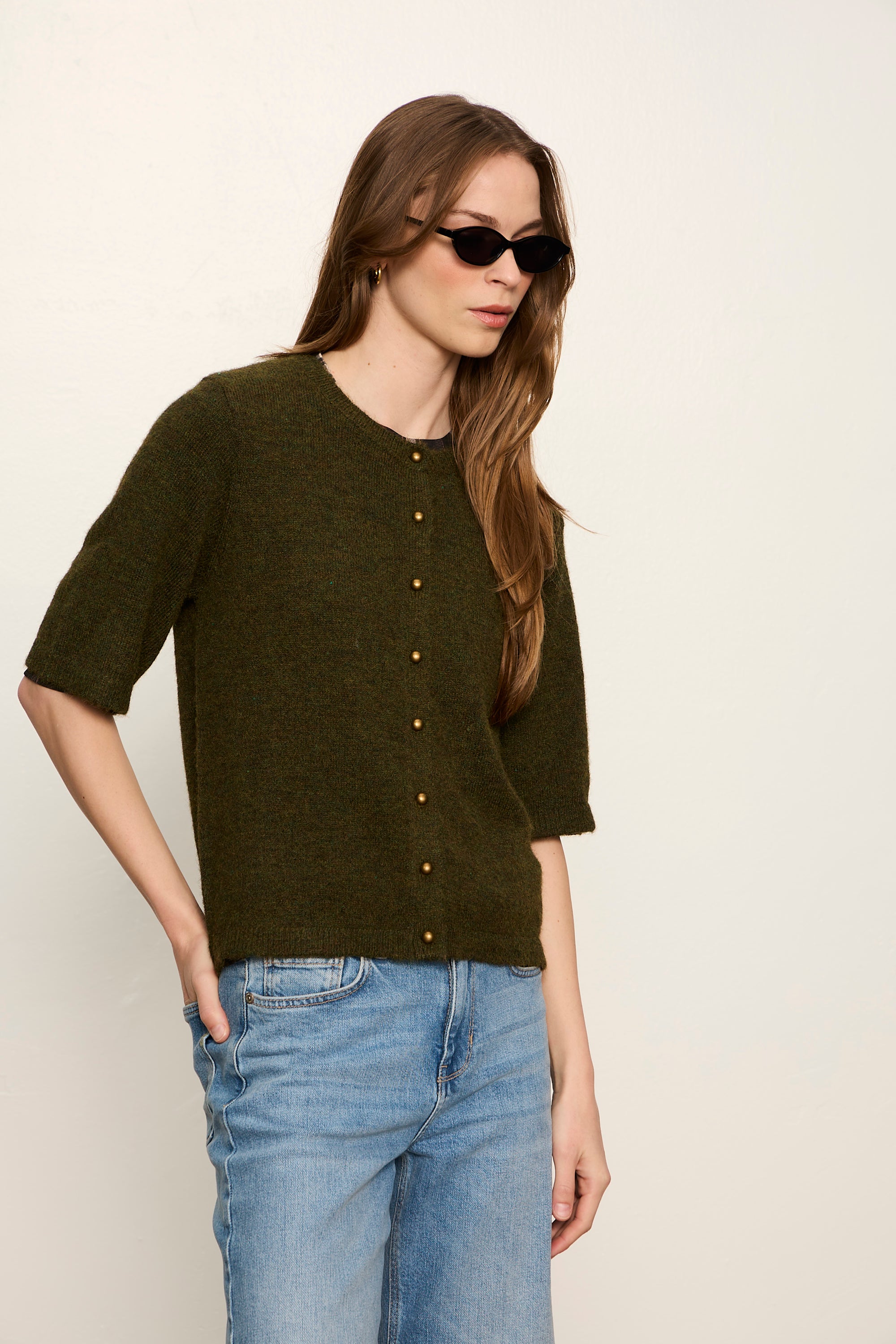 Woman wearing a dark green sweater and blue jeans against a plain background