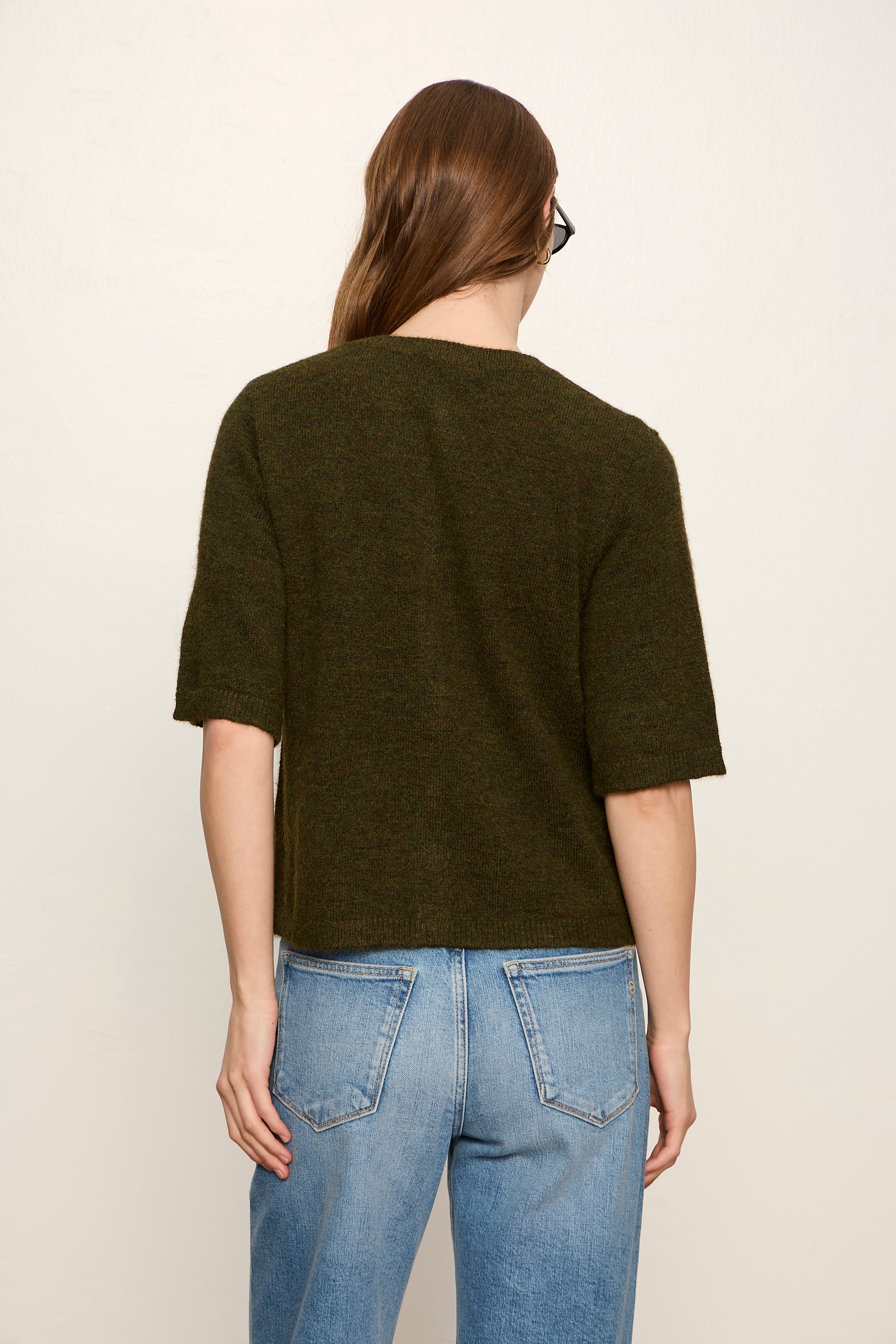 Person wearing a dark green t-shirt and blue jeans on a plain background