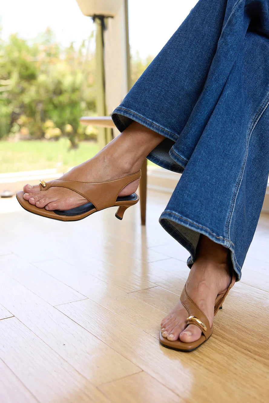 Person wearing brown sandals and blue jeans sitting on a wooden floor.