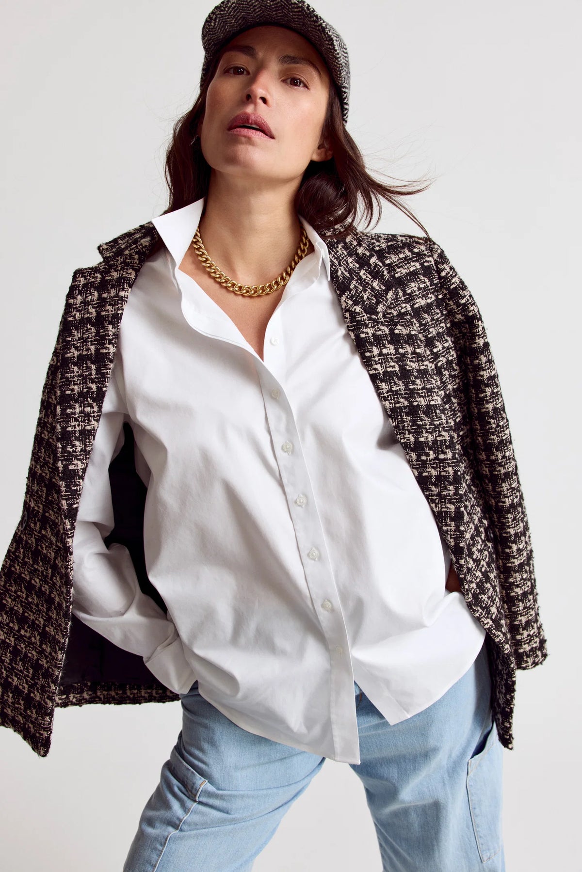 Woman wearing a white shirt, tweed jacket, and cap on a plain background