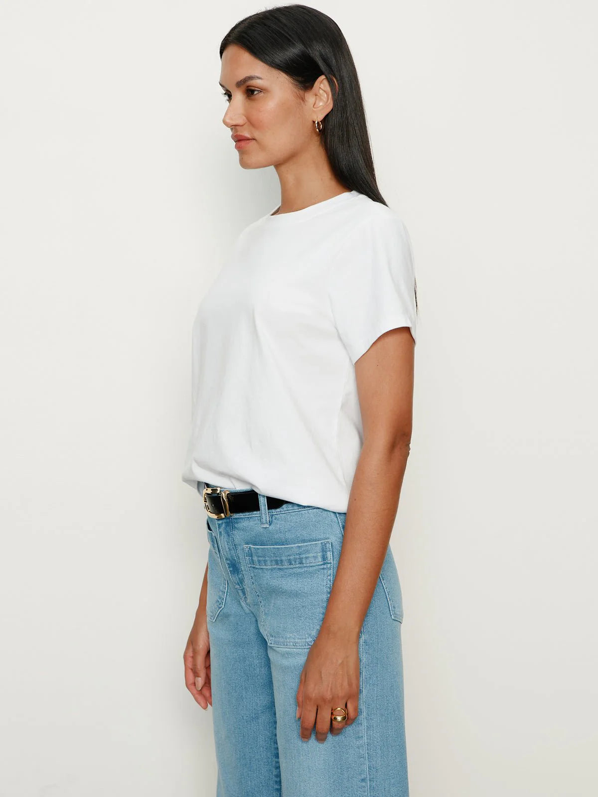Woman wearing a white t-shirt and light blue jeans against a plain background
