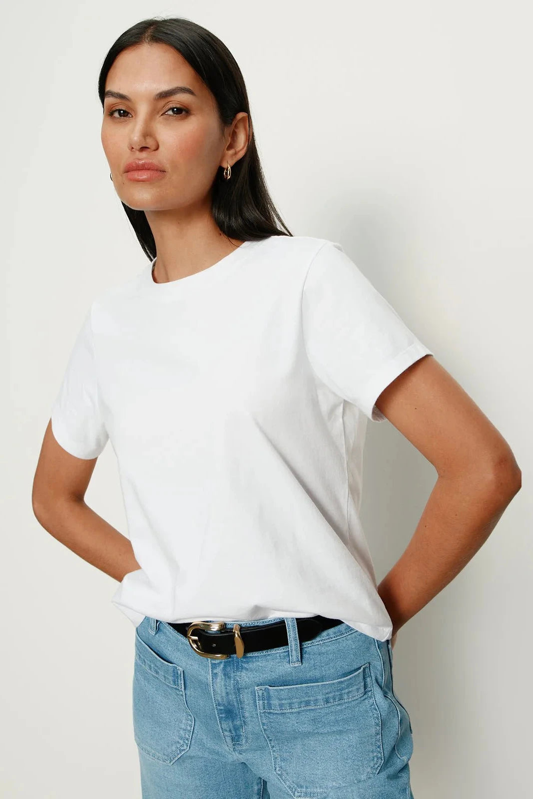 Woman wearing a white t-shirt and blue jeans against a plain background